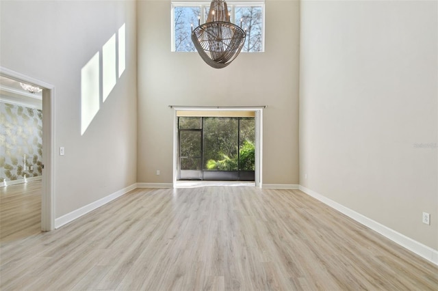 unfurnished living room featuring light wood-type flooring, a towering ceiling, and a notable chandelier