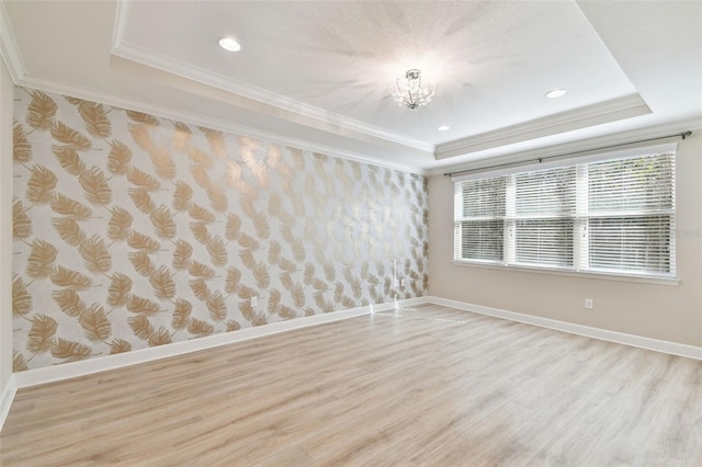 unfurnished room with light hardwood / wood-style flooring, a raised ceiling, ornamental molding, and an inviting chandelier