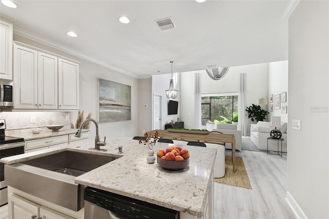 kitchen with appliances with stainless steel finishes, white cabinetry, decorative backsplash, sink, and a kitchen island with sink