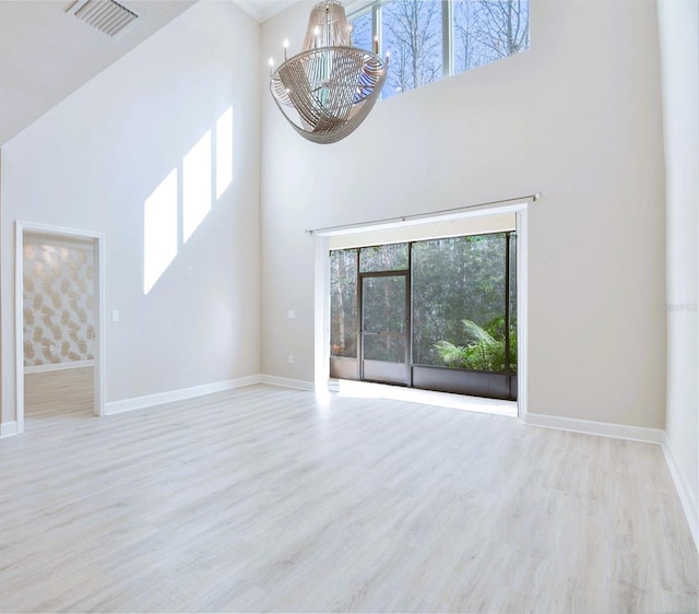 unfurnished living room with an inviting chandelier, a towering ceiling, and light wood-type flooring