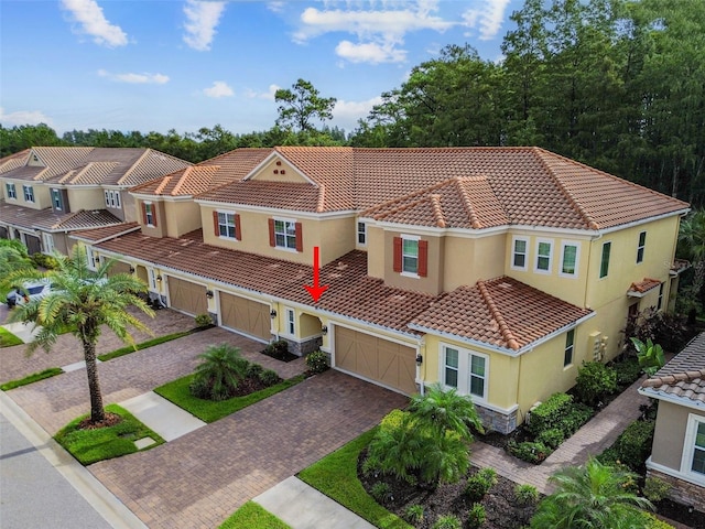 mediterranean / spanish house featuring driveway, stucco siding, stone siding, and a tiled roof