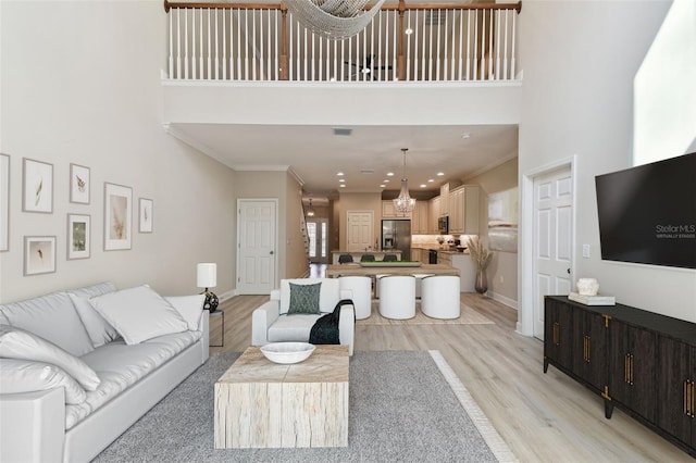 living area with ornamental molding, light wood-style floors, and a high ceiling