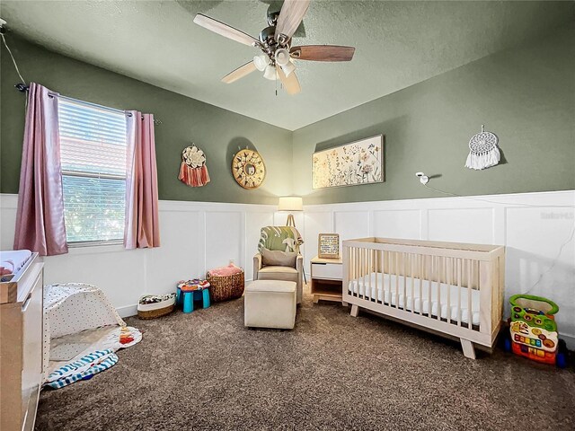 carpeted bedroom with a crib, ceiling fan, and a textured ceiling