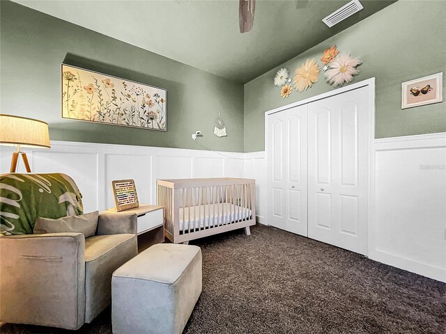 carpeted bedroom featuring ceiling fan, a closet, and a crib