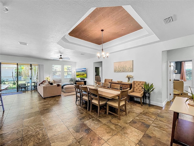 dining room with a tray ceiling, ceiling fan with notable chandelier, and a healthy amount of sunlight