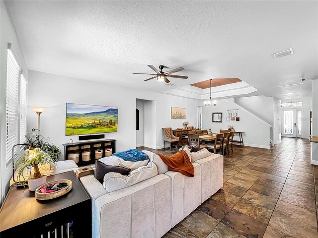 living room featuring ceiling fan with notable chandelier, a raised ceiling, a textured ceiling, and a healthy amount of sunlight