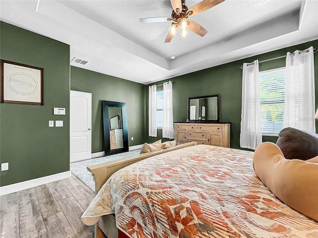 bedroom featuring a textured ceiling, ceiling fan, a tray ceiling, and light hardwood / wood-style floors