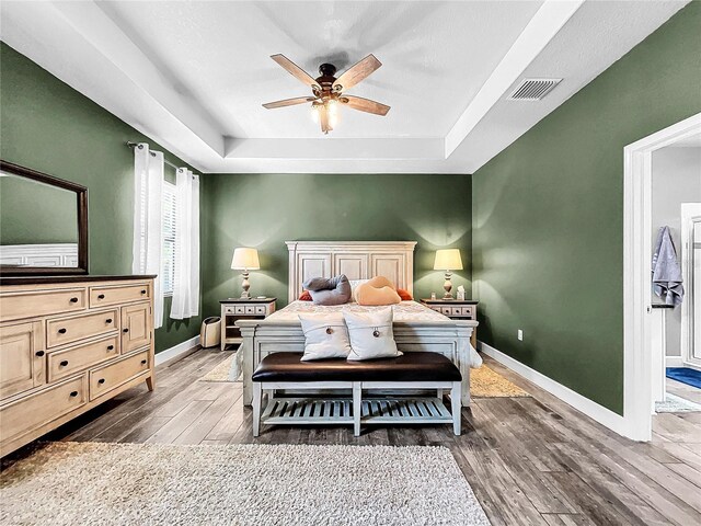 bedroom featuring dark wood-type flooring, a raised ceiling, and ceiling fan