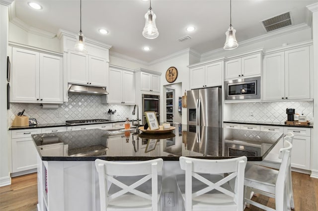 kitchen with pendant lighting, a kitchen island with sink, backsplash, stainless steel appliances, and a breakfast bar