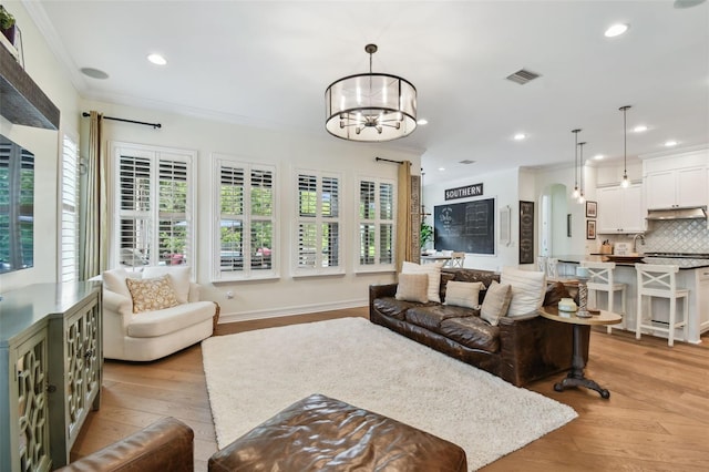 living room with an inviting chandelier, light wood-type flooring, and crown molding