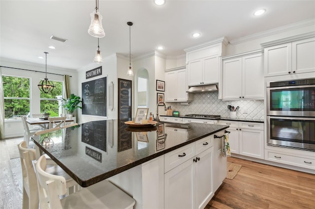 kitchen featuring an island with sink, appliances with stainless steel finishes, light wood-type flooring, and hanging light fixtures