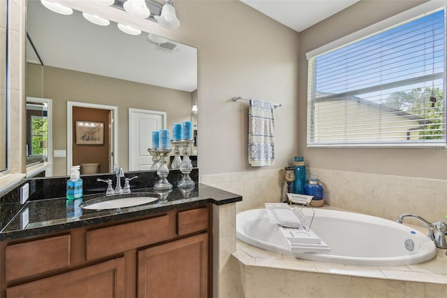 bathroom featuring tiled tub, vanity, and plenty of natural light