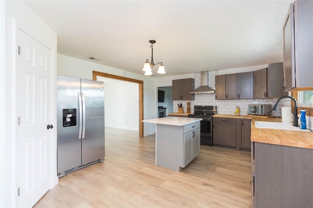 kitchen featuring a kitchen island, wall chimney exhaust hood, appliances with stainless steel finishes, sink, and a chandelier