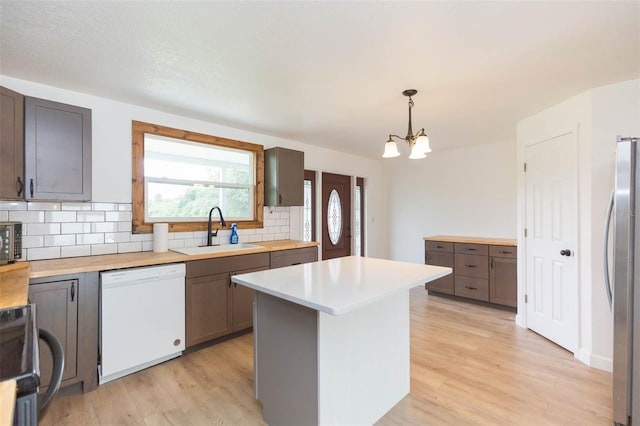 kitchen with white dishwasher, light hardwood / wood-style floors, stainless steel refrigerator, sink, and a chandelier