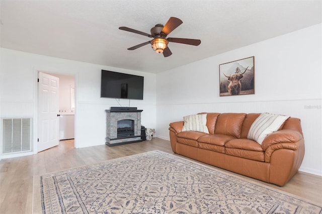 living room with light wood-type flooring, ceiling fan, a fireplace, and a textured ceiling