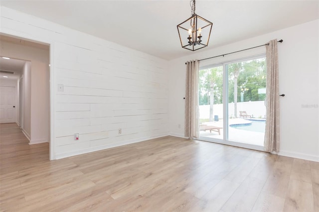 spare room featuring an inviting chandelier and light hardwood / wood-style floors