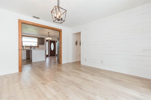 unfurnished room with an inviting chandelier, sink, and light hardwood / wood-style floors