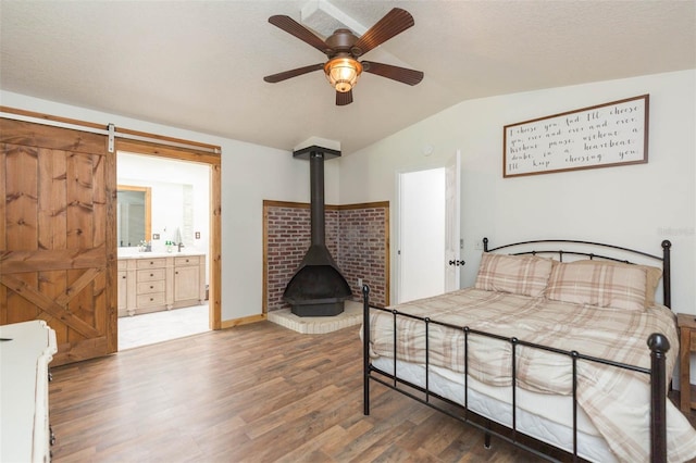 bedroom with connected bathroom, a wood stove, ceiling fan, dark wood-type flooring, and lofted ceiling