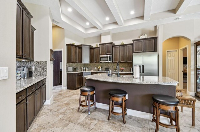 kitchen with tasteful backsplash, stainless steel appliances, light stone countertops, and a center island with sink