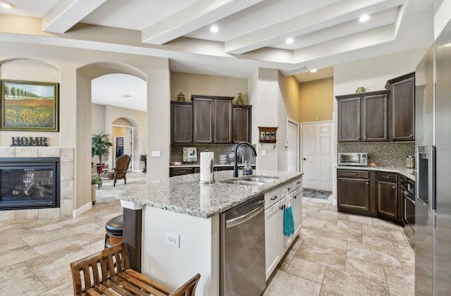 kitchen featuring a fireplace, appliances with stainless steel finishes, light stone countertops, sink, and tasteful backsplash