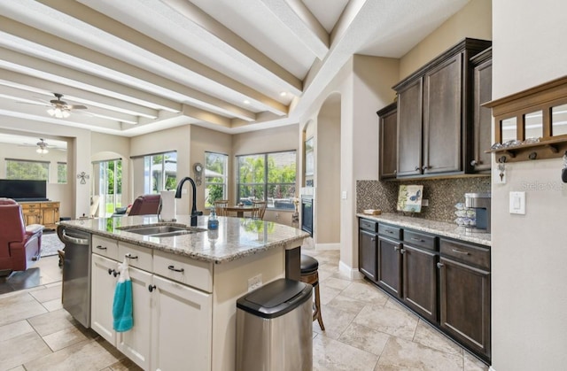 kitchen with light stone countertops, a center island with sink, sink, ceiling fan, and white cabinets