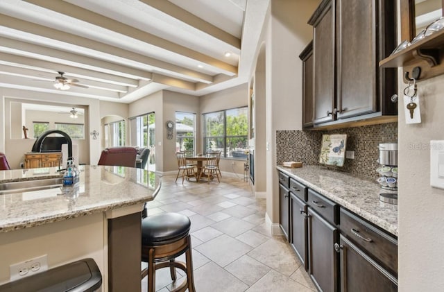 kitchen featuring ceiling fan, light stone counters, dark brown cabinets, and sink