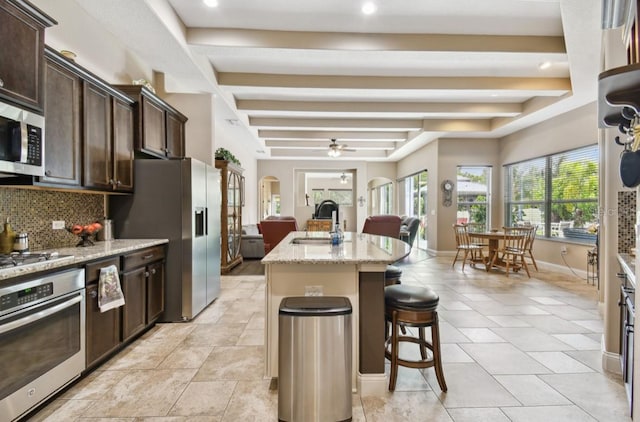 kitchen with appliances with stainless steel finishes, light stone countertops, sink, an island with sink, and a breakfast bar area