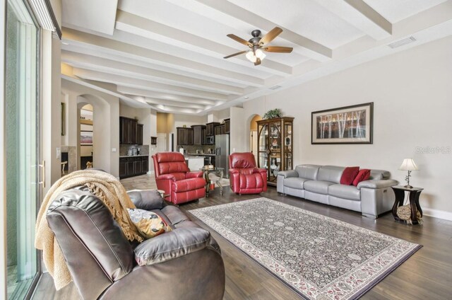 living room featuring dark wood-type flooring, ceiling fan, and beam ceiling