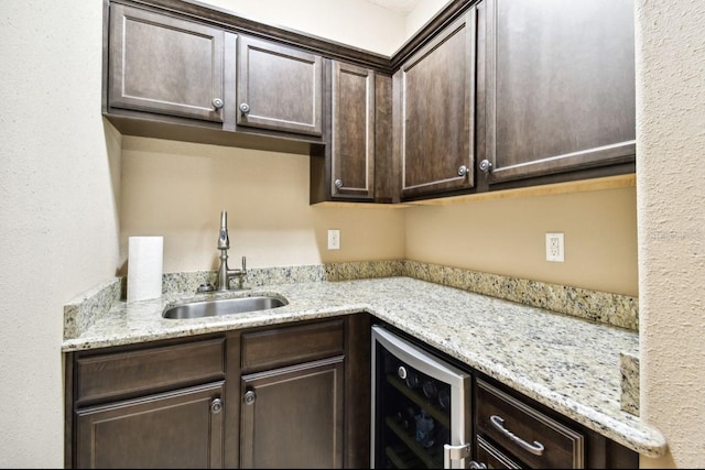 kitchen featuring light stone counters, wine cooler, sink, and dark brown cabinetry