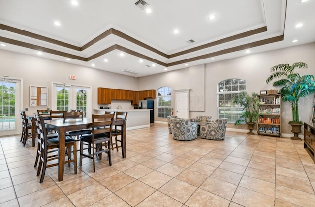 dining space with a tray ceiling, ornamental molding, light tile patterned floors, and a high ceiling