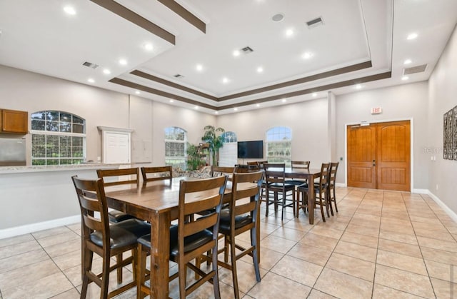 tiled dining room featuring crown molding, a healthy amount of sunlight, and a raised ceiling