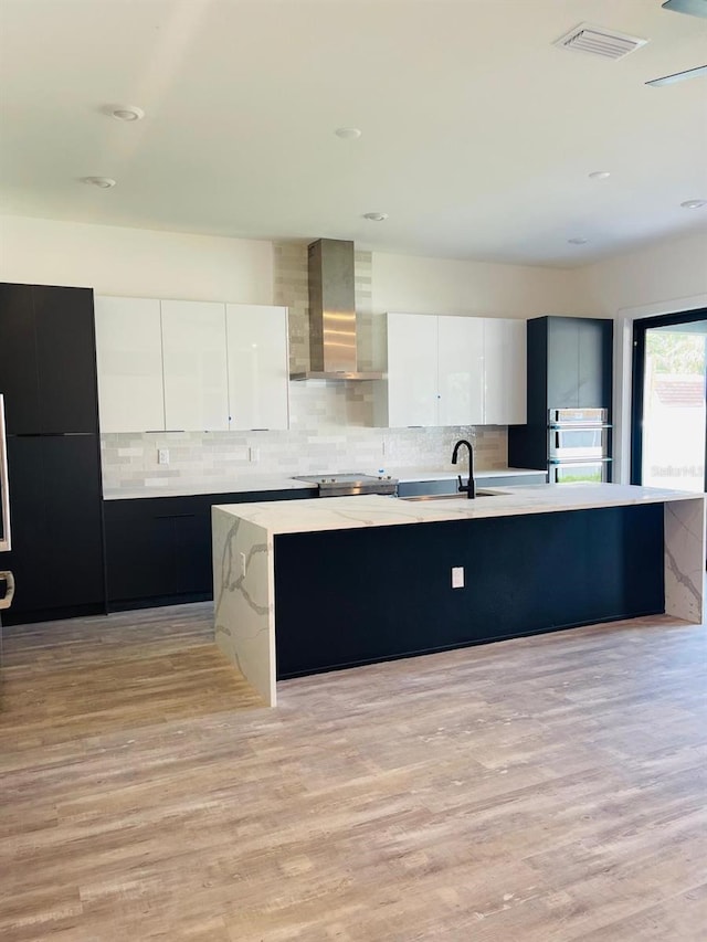 kitchen featuring white cabinets, light hardwood / wood-style floors, a kitchen island with sink, and wall chimney exhaust hood