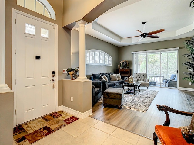 foyer with a tray ceiling, ornate columns, ceiling fan, and light hardwood / wood-style floors