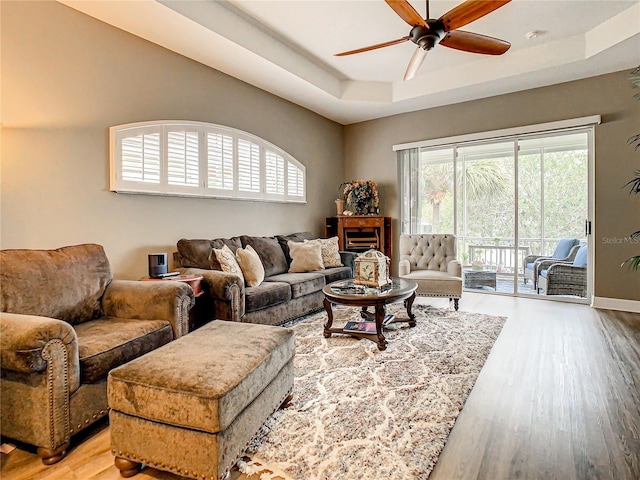 living room featuring a raised ceiling, wood-type flooring, and ceiling fan