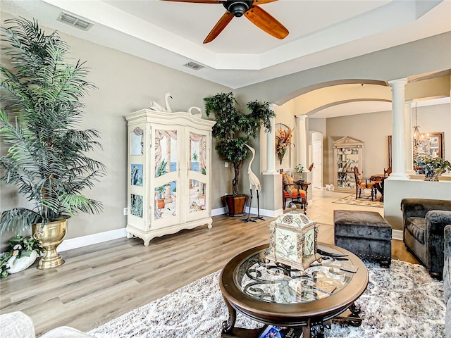 living room with light hardwood / wood-style flooring, decorative columns, a raised ceiling, and ceiling fan