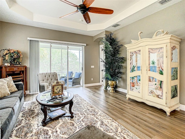 living room featuring a tray ceiling, ceiling fan, and wood-type flooring