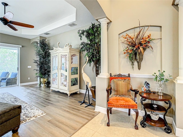 sitting room with ceiling fan, a tray ceiling, hardwood / wood-style flooring, and ornate columns