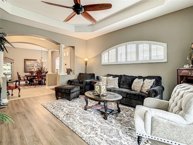 4737 Casswell Dr, New Port Richey, FL 34652 - living room featuring decorative columns, arched walkways, ceiling fan, a tray ceiling, and light wood-type flooring