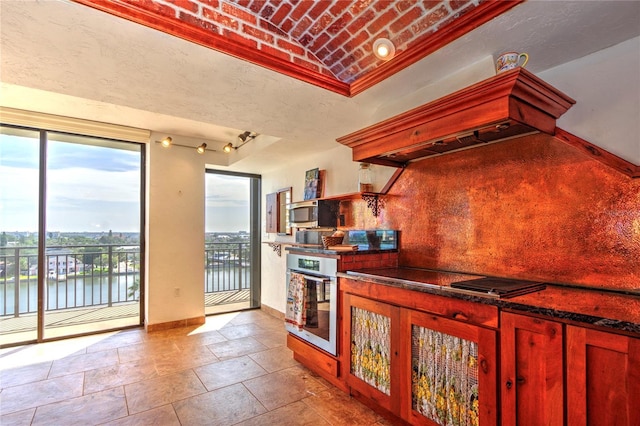 kitchen with baseboards, a water view, brick ceiling, stone tile flooring, and stainless steel oven