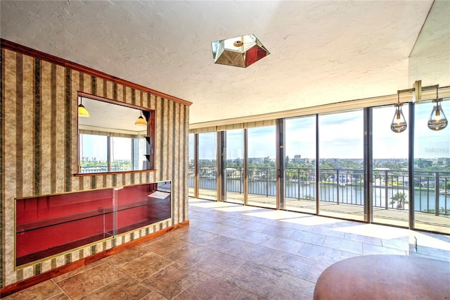 interior space with a textured ceiling, a wall of windows, a water view, and stone tile flooring