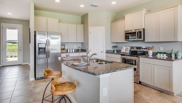 kitchen with a breakfast bar area, a center island with sink, appliances with stainless steel finishes, sink, and dark stone counters