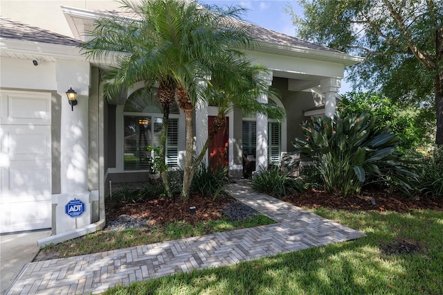 view of exterior entry featuring stucco siding and a shingled roof