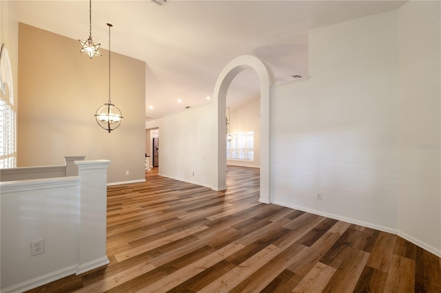 empty room with arched walkways, recessed lighting, baseboards, and wood finished floors