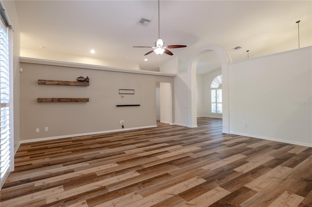 empty room featuring a ceiling fan, wood finished floors, visible vents, recessed lighting, and arched walkways