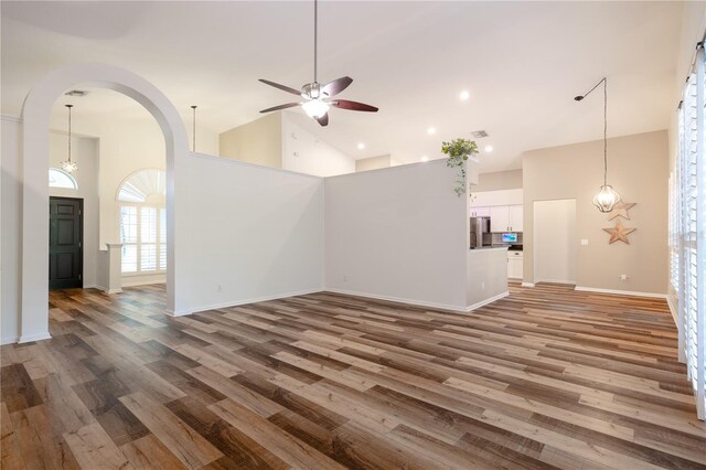 unfurnished living room with ceiling fan, wood finished floors, arched walkways, and high vaulted ceiling