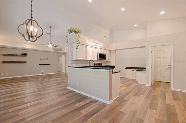 kitchen featuring a ceiling fan, stainless steel microwave, dark countertops, white cabinetry, and light wood finished floors