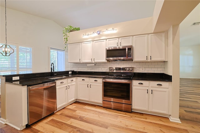 kitchen with lofted ceiling, a peninsula, a sink, stainless steel appliances, and light wood-style floors