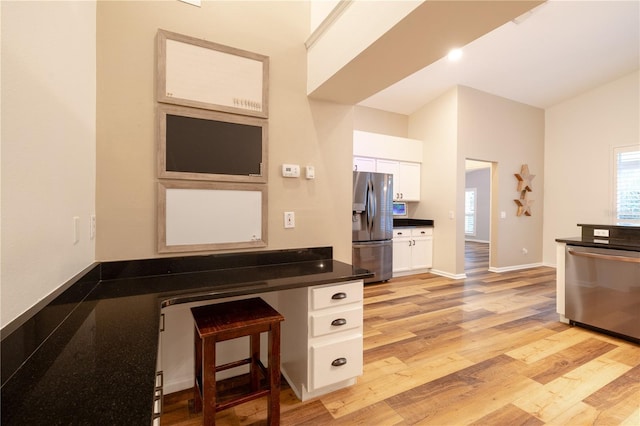 kitchen featuring dark countertops, light wood finished floors, a kitchen breakfast bar, stainless steel appliances, and white cabinetry