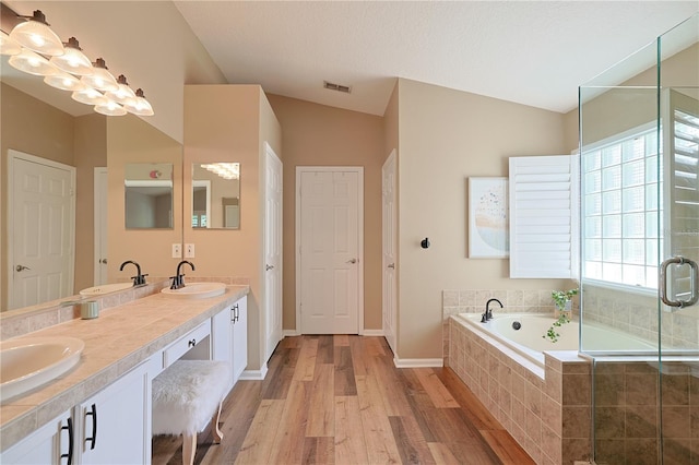 full bathroom featuring visible vents, vaulted ceiling, wood finished floors, a bath, and a sink