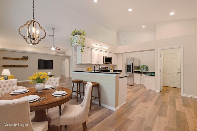 kitchen featuring light wood finished floors, a peninsula, appliances with stainless steel finishes, white cabinetry, and dark countertops